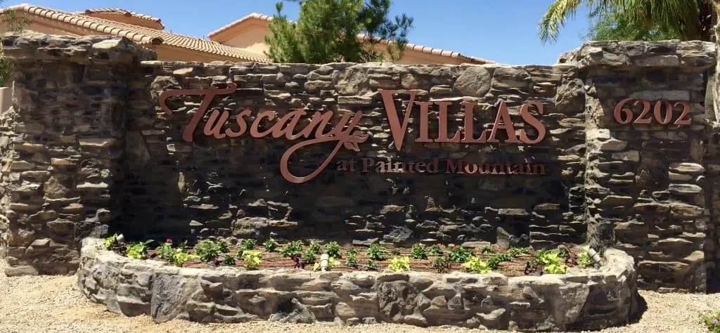 Tuscany Villas entrance sign at Painted Mountain, featuring stone wall and landscaped flowers, representing a gated resort-style community in Mesa, AZ.